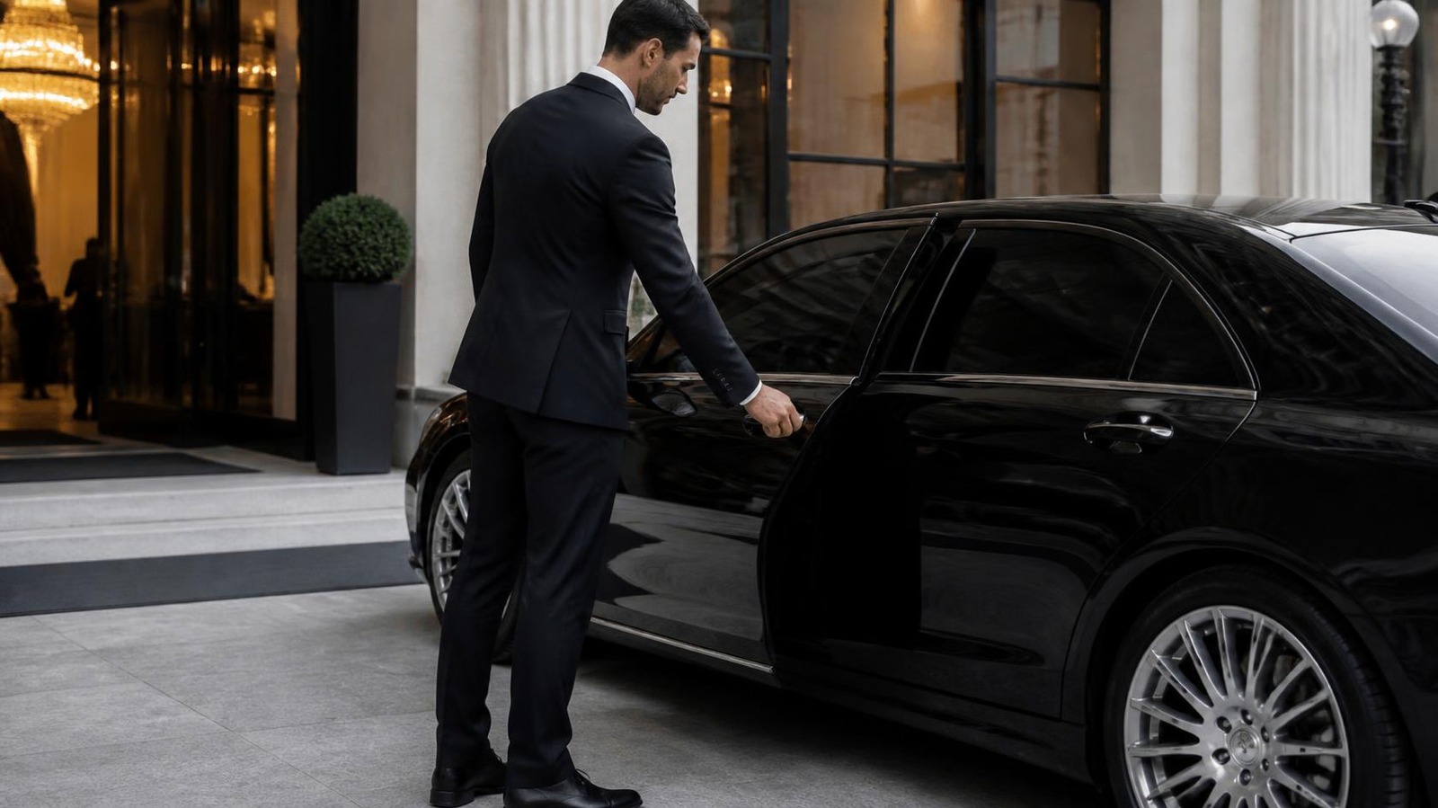 Chauffeur opening the door of a black sedan for a VIP